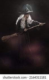 Halloween. Full Length Portrait Of An Ugly Old Witch Standing With Her Magic Broom On A Black Backgroung. Witchcraft.