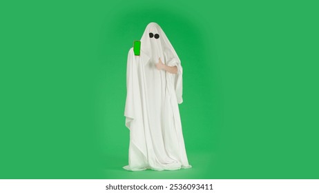 Halloween ghost in white sheet showing smartphone mockup, thumb up at camera, isolated on chroma key green screen background, full length. Spooky concept. - Powered by Shutterstock