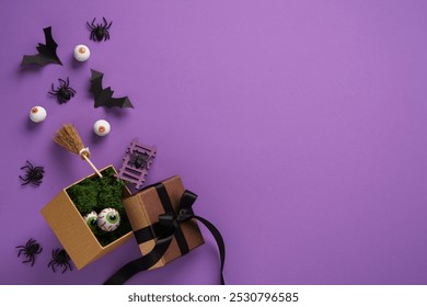 Halloween gift box with spooky decorations: fake eyeballs, bats, spiders, and broomstick on purple background. Space for your text, announcement, invitation. - Powered by Shutterstock