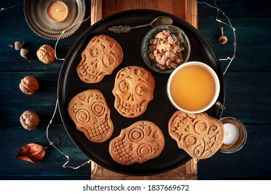 Halloween Ginger Cookies In The Shape Of Skulls, Homemade Dia De Los Muertos Biscuits, With Tea And Candles, Shot From Above On A Dark Wooden Background