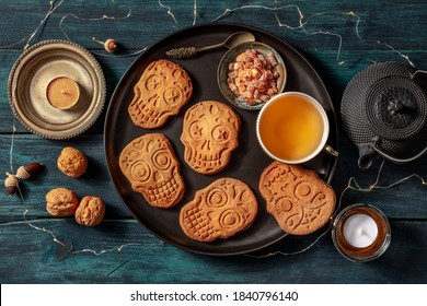 Halloween Ginger Cookies In The Shape Of Skulls, Homemade Dia De Los Muertos Biscuits, Shot From Above With Tea And Candles On A Dark Wooden Background