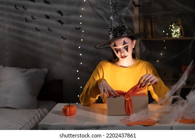 Halloween Girl In Witch Hat Holding A Paper Craft Gift Box And Satin Ribbon Bow On Table With Copy Space, Discount, Sale Flyer, Minimal Concept, Papercraft Wrapping Of Present, Halloween Sale Concept