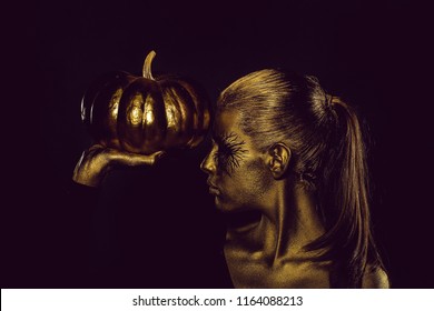 Halloween Golden Woman Or Girl Holding Painted Gold Pumpkin Has Pretty Face With Makeup And Body Art Metallized Color On Black Background