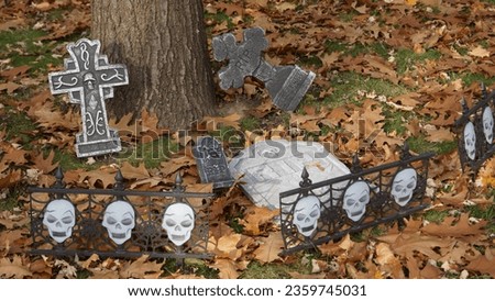 Halloween graveyard. Skulls, fence, cross, tomb, cemetry at bottom of tree on dry leaves ground. RIP. Halloween outside decorations. - 30 October 2022, Montreal, Canada