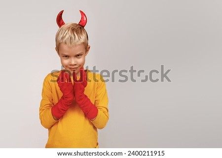 Halloween Happy child laughs out loud with devilish horns in a yellow turtleneck against a gray studio background. Happy Halloween holidays concept