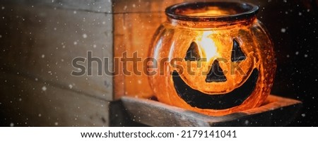 Halloween head jack pumpkin glass lantern with burning candle and old wooden table background with snow fall.Scary halloween festival holiday concept.