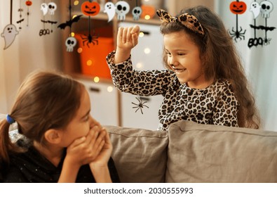 halloween, holiday and childhood concept - smiling little girls in party costumes playing with toy spider at home decorated with garland and lights - Powered by Shutterstock