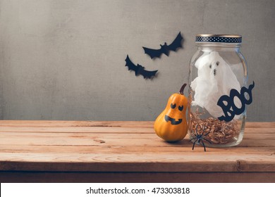 Halloween holiday decoration with ghost in jar and pumpkin with scary face on wooden table