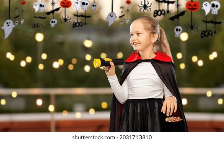 Halloween, Holiday And Trick-or-treating Concept - Happy Smiling Girl In Black Dracula Cape Or Costume With Candies And Flashlight Over Roof Top Party And Decorations On Background