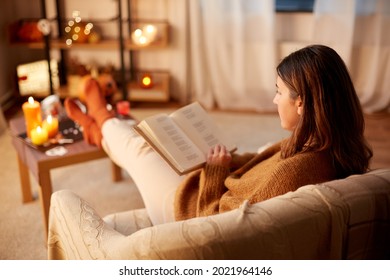 halloween, holidays and leisure concept - young woman reading book and resting her feet on table at cozy home - Shutterstock ID 2021964146