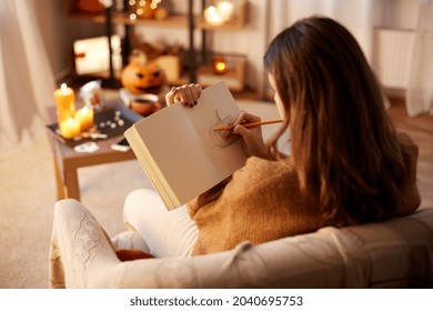 halloween  holidays   leisure concept    young woman and pencil drawing in sketchbook diary   resting her feet table at cozy home