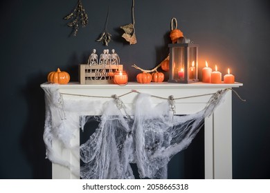 Halloween home decoration. Plastic toy skeletons in a wooden box on a fireplace against a dark blue wall. A garland of skeletons. Cobweb on the dresser. Orange candles and lantern. - Powered by Shutterstock
