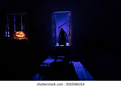 Halloween Horror Concept With Glowing Pumpkin. A Realistic Dollhouse Living Room With Furniture, Door And Window At Night. Grim Reaper On Door With Blade. Selective Focus.