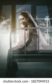 Halloween Horror Concept. Horrible Female Bride Ghost With Wounded Face Sitting On The Bed With Modern City View Background On The Window