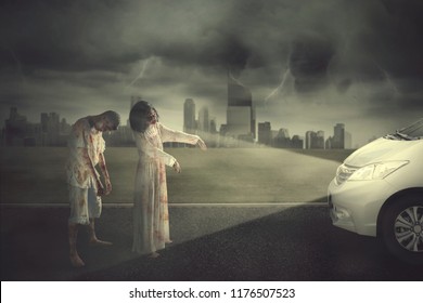 Halloween horror concept. Two horrible zombies attacking a car at night time. Shot with city background