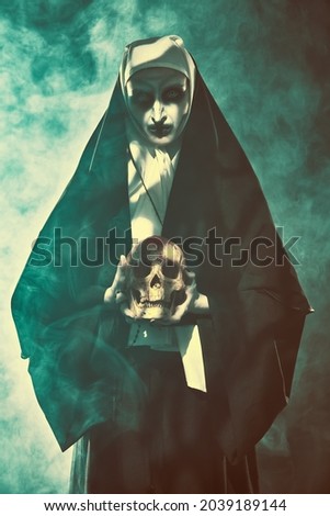Halloween and Horrors. Devilish evil nun holds a skull in her hands standing in mysterious haze.