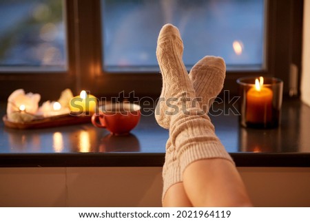halloween, hygge and leisure concept - legs in socks on window sill at home in autumn
