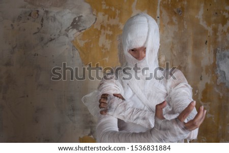 Halloween image, mummy in bandages, risen dead legendary character. young woman in the form of a mummy wrapped in bandages, against the textured old wall
