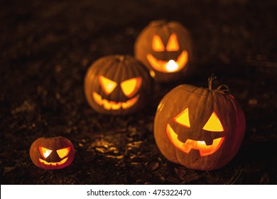 Halloween jack-o-lantern pumpkins on ground with brown autumn leaves