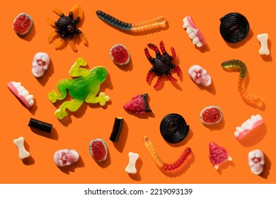 Halloween jelly beans in the shape of worms, skulls, frogs, vampire teeth, brains, bones, spiders, licorice spirals on orange background with hard shadow. Festive sweets pattern, gummy trick or treat. - Powered by Shutterstock