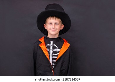 Halloween kids A boy in a skeleton costume holds a jack o lantern. Black background. Copy space A child in a black coat hat holds a halloween pumpkin. Place for text. - Shutterstock ID 2187214567