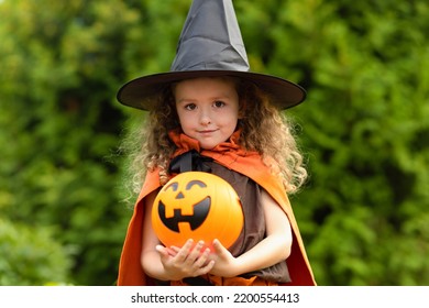 Halloween Kids. Portrait Happy Girl In Witch Costume, Black Hat On Scary Merry Holiday. Child With Pumpkin, Jack O Lantern, Basket Candy Sweet, Scaring Boo