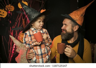 Halloween Man And Child In Witch Hat. Boy Kid With Happy Face And Bearded Man At Pumpkin. Party And Celebration. Halloween Holiday And Celebration. Father And Small Son Drink From Tea Or Milk Cup.