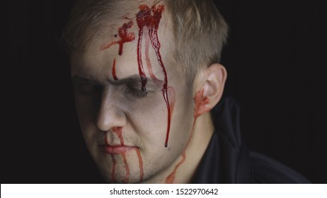 Halloween man portrait with head injury. Guy with dripping blood on his face. Executioner, Vampire makeup. Fashion art design. Attractive model in Halloween costume. Dark black background