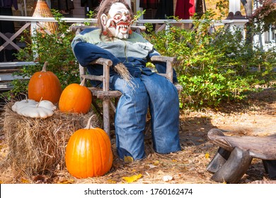 Halloween Mannequin In With Ugly Mask Chair Outside Beside Three Large Orange Pumpkins.