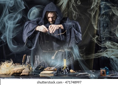 Halloween. The medieval alchemist holds magic ritual at the table in his laboratory smoke in the background