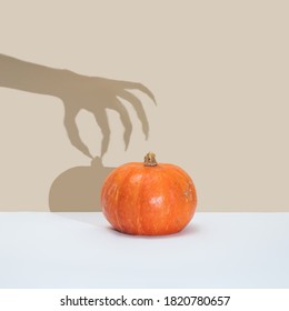 Concept minimal d'Halloween avec citrouille et ombre de sorcière ou de main zombie. Arrière-plan amusant et créatif