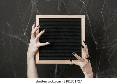 Halloween mock up. Letter board in hands with long black nails and spider ring on black background with spiderweb. Front view. - Powered by Shutterstock