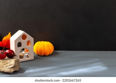 Halloween. On A Black And Gray Background Stands A House With A Fire Inside. Next To It Lie A Pumpkin And Small Apples On A Stone