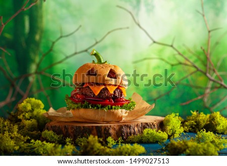 Halloween party burger in shape of scary pumpkin  on natural wooden board. Halloween food concept.
