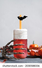 Halloween party concept. Skeleton hand holding a glass of red Halloween cocktail with cold foam.