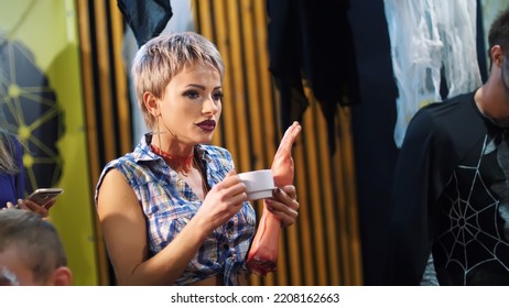 Halloween Party, A Girl Drinks From A Cup Something, Her Lips Are Sewn, She Holds A Bloody Human Hand. High Quality Photo