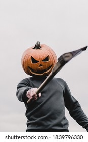 Halloween person wearing a pumpkin head swinging an axe