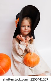 Halloween Portrait Of A Little Girl In A Witch Magic Hat. Little Child With Pumpkins. White Background. 