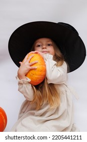 Halloween Portrait Of A Little Girl In A Witch Magic Hat. Little Child With Pumpkins. White Background. 