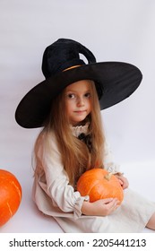 Halloween Portrait Of A Little Girl In A Witch Magic Hat. Little Child With Pumpkins. White Background. 