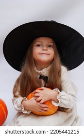 Halloween Portrait Of A Little Girl In A Witch Magic Hat. Little Child With Pumpkins. White Background. 