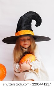 Halloween Portrait Of A Little Girl In A Witch Magic Hat. Little Child With Pumpkins. White Background. 