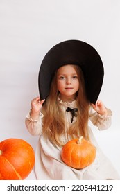 Halloween Portrait Of A Little Girl In A Witch Magic Hat. Little Child With Pumpkins. White Background. 