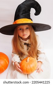 Halloween Portrait Of A Little Girl In A Witch Magic Hat. Little Child With Pumpkins. White Background. 