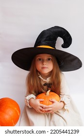 Halloween Portrait Of A Little Girl In A Witch Magic Hat. Little Child With Pumpkins. White Background. 