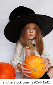 Halloween Portrait Of A Little Girl In A Witch Magic Hat. Little Child With Pumpkins. White Background. 