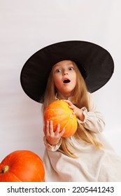 Halloween Portrait Of A Little Girl In A Witch Magic Hat. Little Child With Pumpkins. White Background. 