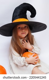 Halloween Portrait Of A Little Girl In A Witch Magic Hat. Little Child With Pumpkins. White Background. 