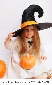 Halloween Portrait Of A Little Girl In A Witch Magic Hat. Little Child With Pumpkins. White Background. 