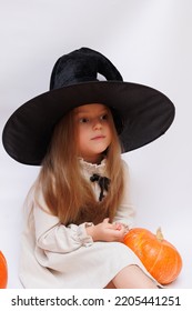 Halloween Portrait Of A Little Girl In A Witch Magic Hat. Little Child With Pumpkins. White Background. 